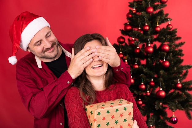 Surpresa romântica no Natal, mulher bonita recebe presente do namorado, homem fecha os olhos da menina com as mãos.