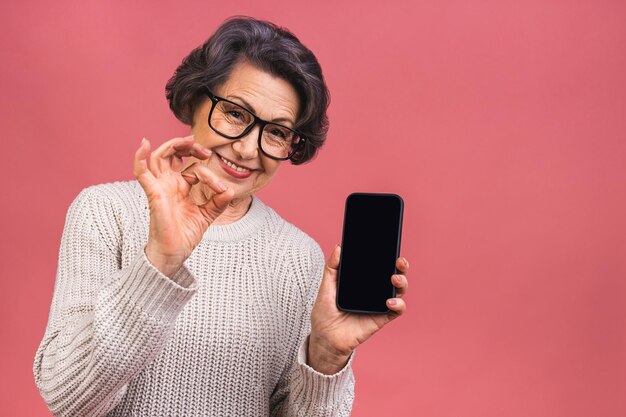 Foto surpresa sorrindo feliz mulher madura sênior mostrando a tela do smartphone em branco