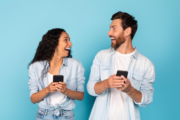 Surpreso feliz e animado jovem casal diversificado com smartphones olha um para o outro se alegrar com a vitória online