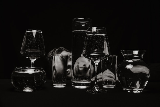 Surrealista retrato en blanco y negro de un hombre mirando a través de vasos de agua sobre un fondo negro
