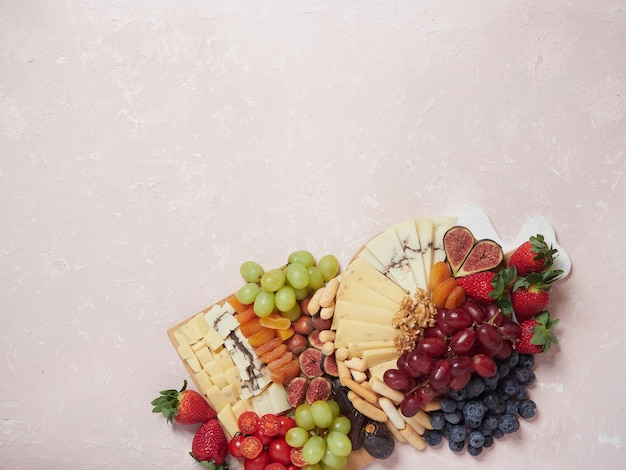 Surtido de aperitivos y aperitivos plato de queso y fruta en tablero de madera sobre fondo rosa Vista superior espacio de copia