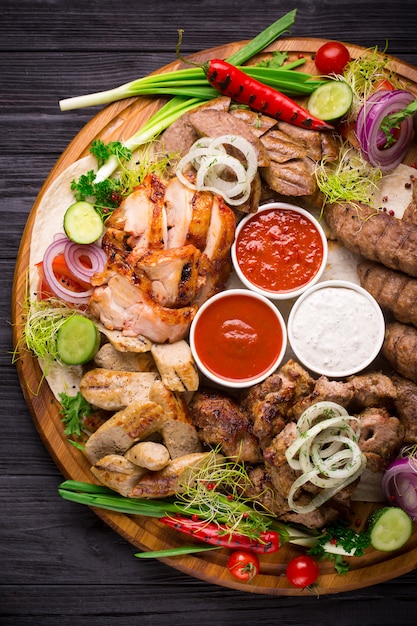 Surtido de carnes a la brasa y verduras en mesa rústica.