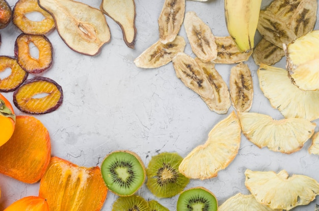 Surtido de chips secos y frutas maduras sobre fondo gris. Chips de frutas. Concepto de alimentación saludable, merienda, sin azúcar. Vista superior, espacio de copia.