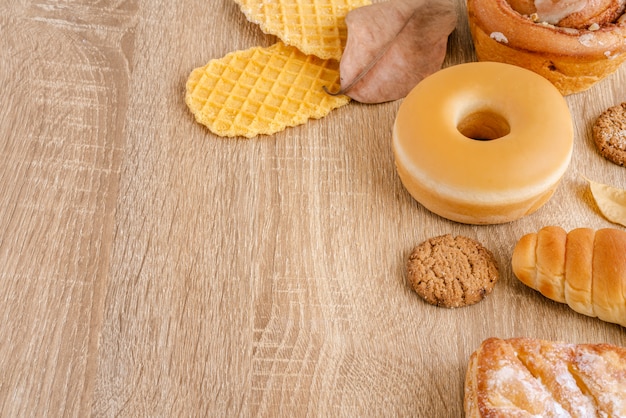 Surtido de donas, gofres crujientes, pan horneado y pasteles en la superficie de la mesa de madera