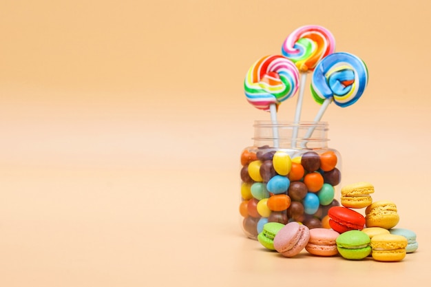 Surtido de dulces en un frasco y pastel de macarrones franceses sobre fondo de color crema con espacio de copia