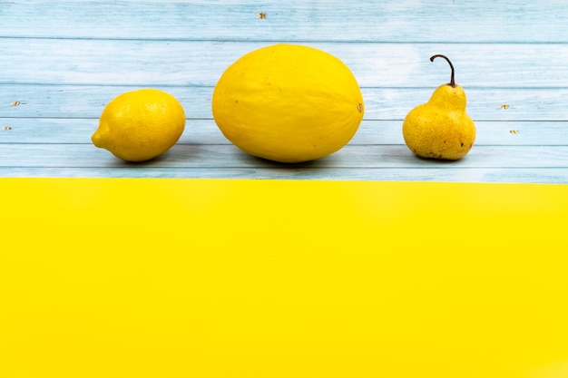 Un surtido de frutas amarillas se encuentra sobre un fondo de madera azul y un fondo amarillo