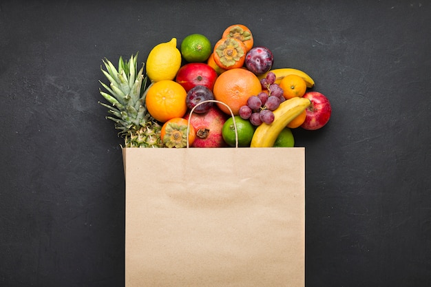 Surtido de frutas en una bolsa de papel sobre hormigón negro. Concepto de vitaminas en la dieta humana.