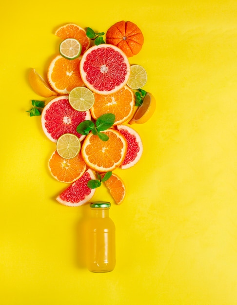 surtido de frutas cítricas, una botella de jugo, sobre un fondo amarillo, ningún pueblo, vertical