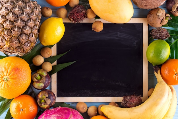 Surtido de frutas tropicales con hojas de palmeras y pizarrón.