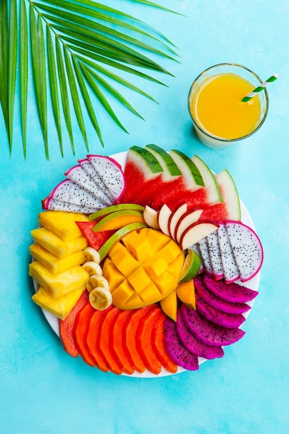 Surtido de frutas tropicales en un plato blanco con jugo de batido de mango Fondo azul Vista superior