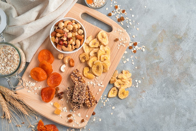 Un surtido de frutos secos, nueces, barras de granola y cereales en una pared gris con espacio para copiar. Aperitivos naturales y saludables.