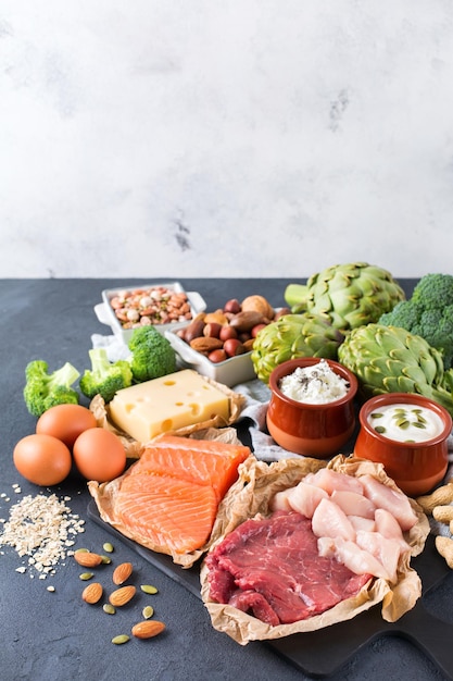 Foto surtido de fuentes de proteínas saludables y alimentos para el desarrollo del cuerpo carne de res salmón pechuga de pollo huevos productos lácteos queso yogur frijoles alcachofas brócoli nueces avena fondo del espacio de copia