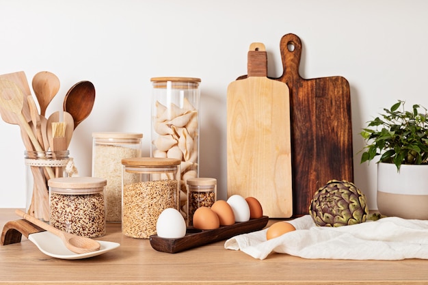 Surtido de granos, cereales y pastas en frascos de vidrio y utensilios de cocina sobre mesa de madera