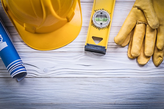 Surtido de guantes de trabajo, casco de construcción, planos laminados en azul, nivel de construcción en tablero de madera