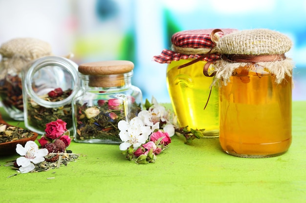 Surtido de hierbas y té y miel en frascos de vidrio sobre mesa de madera sobre fondo brillante