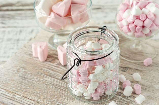 Surtido de malvaviscos rosados y blancos en vasos de vidrio sobre fondo de madera. Malvavisco en forma de corazón para chocolate caliente o cacao.