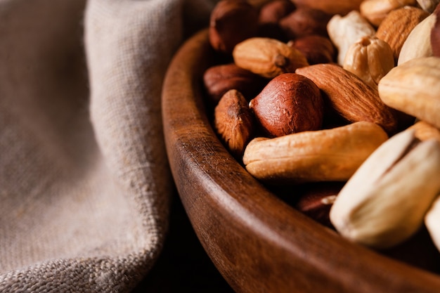 Surtido de nueces en recipiente de madera sobre mesa de madera oscura. Anacardos, avellanas, almendras y pistachos.