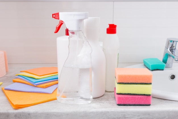 Surtido de nuevos productos de limpieza para el hogar dispuestos junto al lavabo en un baño con paños, recipientes, dispensadores y esponjas de colores.