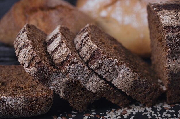 Surtido de pan horneado sobre fondo oscuro. Pan de centeno en rodajas. Concepto de tienda de alimentos de panadería y abarrotes.