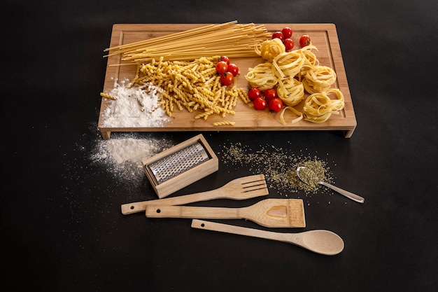 Surtido de pasta cruda italiana de harina de trigo con tomates cherry y utensilios de cocina de madera