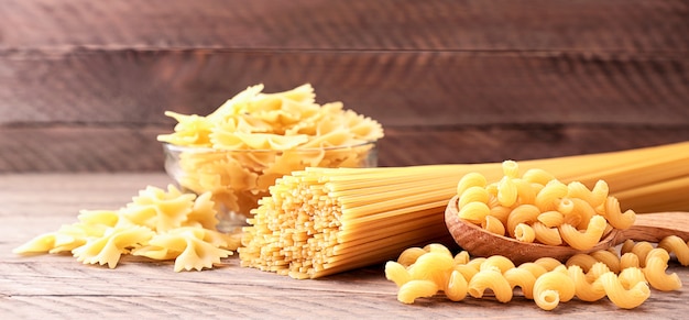 Surtido de pasta de espaguetis, mariposas, rizos en primer plano de fondo de madera