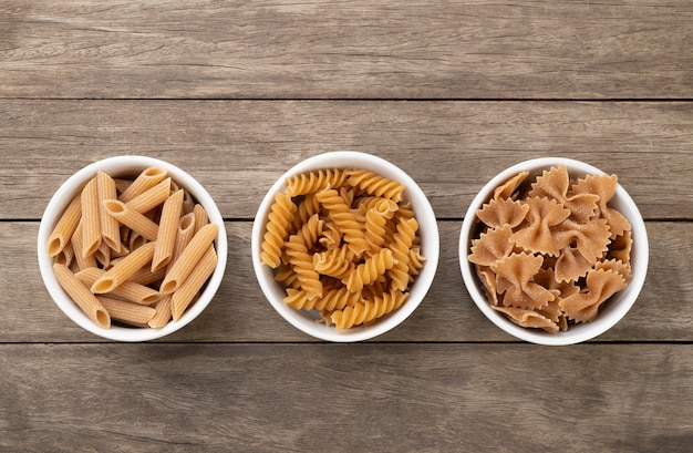 Foto surtido de pasta de trigo integral en tazones sobre mesa de madera.