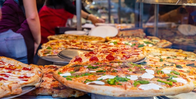 Surtido de pizzas italianas en una exhibición de tienda Trabajadoras sirviendo las pizzas