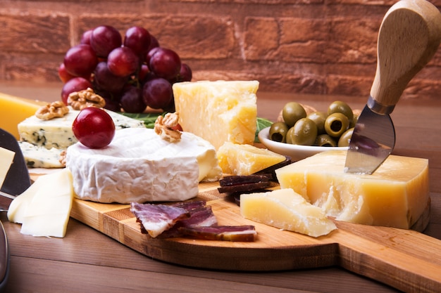 Surtido de queso con frutas, uvas, nueces y cuchillo de queso en una bandeja de madera.