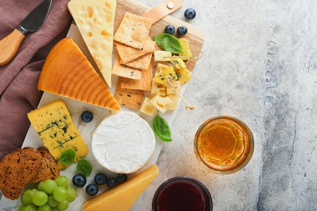 Surtido de queso miel cracker arándanos uvas con vino tinto y blanco en copas servidor antipasto en tablero de mármol blanco sobre fondo gris Espacio de copia plana