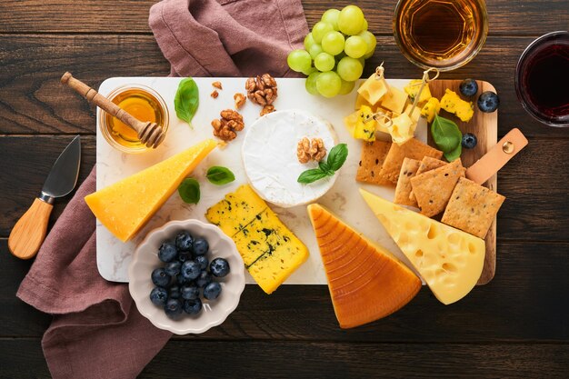 Surtido de queso miel galleta arándanos uvas con vino tinto y blanco en copas servidor antipasto en tablero de mármol blanco sobre fondo de mesa de madera rústica antigua Espacio de copia plana