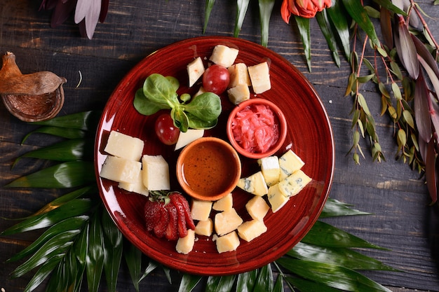 Surtido de quesos con fresas, uvas y salsa. En un plato rojo. Con decoración floral