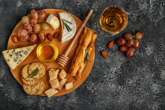 Surtido de quesos con vino, miel, nueces y uvas en una tabla de cortar.