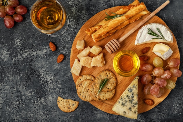 Surtido de quesos con vino, miel, nueces y uvas en una tabla de cortar.