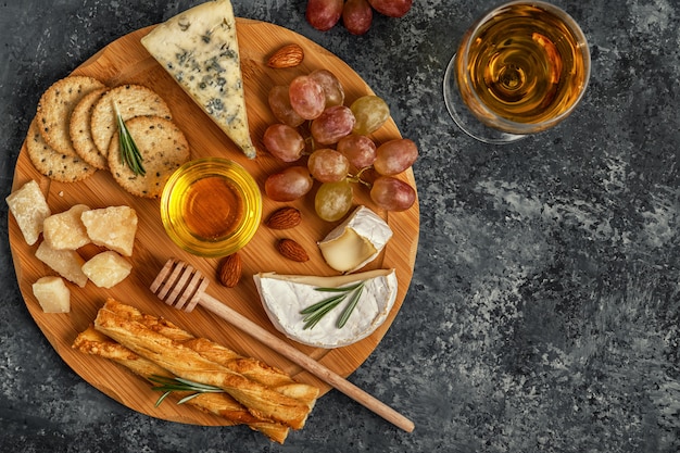 Surtido de quesos con vino, miel, nueces y uvas en una tabla de cortar.