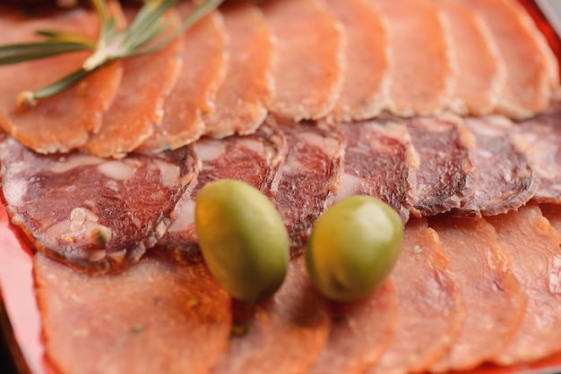 Surtido de salchichas, jamón y jamón con rebanadas de pan frito en un plato rojo. En una mesa de madera