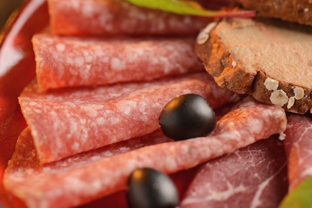 Surtido de salchichas, jamón y jamón con rebanadas de pan frito en un plato rojo. En una mesa de madera