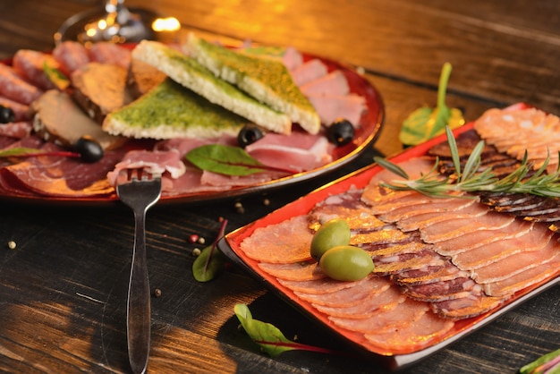 Surtido de salchichas, jamón y jamón con rebanadas de pan frito en un plato rojo. En una mesa de madera