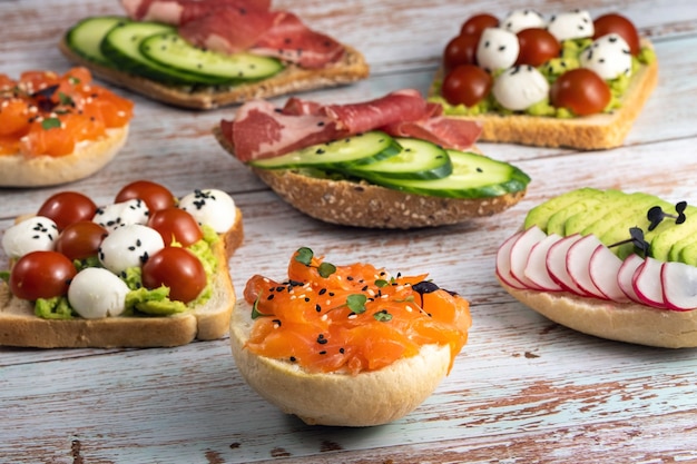 Un surtido de sándwiches con pescado, queso, carne y verduras yacía sobre la mesa de madera