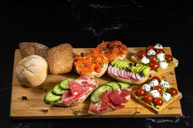 Un surtido de sándwiches con pescado, queso, carne y verduras yacían sobre la tabla y un bollo.