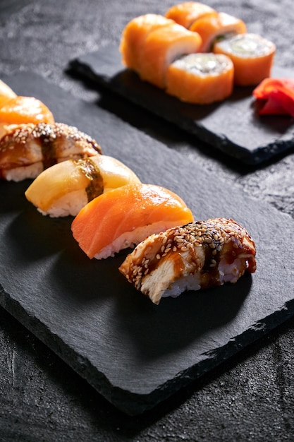 Surtido de sushi con anguila de salmón y escolar en placa de piedra negra sobre fondo oscuro