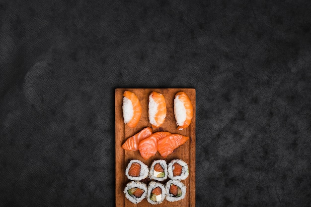 Foto surtido de sushi en bandeja de madera con fondo de textura negro