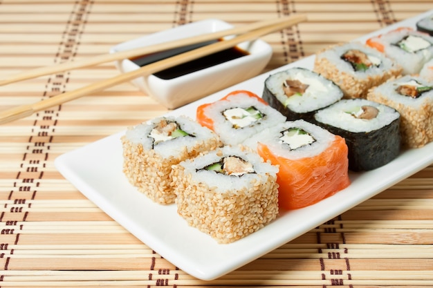 Surtido de sushi en plato blanco, con salsa de soja sobre fondo de bambú.