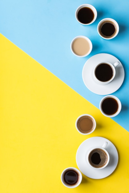 Surtido de tazas de café y tazones con tostado negro, americano, capuchino, leche sobre un fondo amarillo y azul. Espacio de copia de moda creativa endecha plana