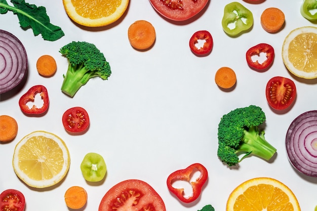 Surtido de verduras y frutas en rodajas sobre superficie blanca.