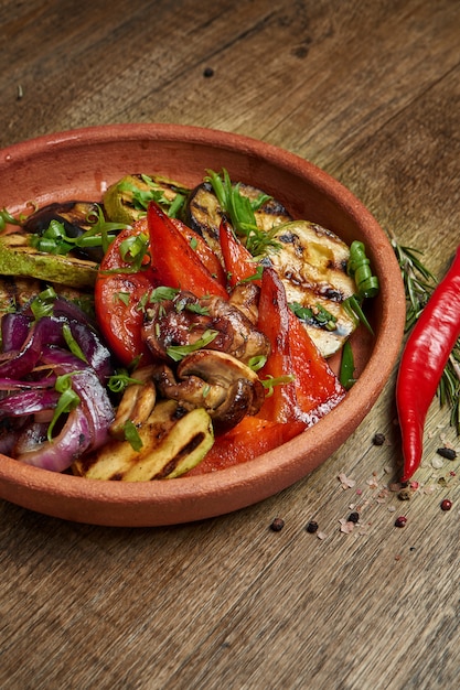 Surtido de verduras a la parrilla: champiñones, calabacín, pimientos, maíz en un plato de cerámica sobre una superficie de madera. Ensalada tibia vegetariana. Comida sana