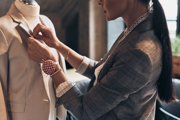 Sus diseños son perfectos. Cerca de joven cosiendo una chaqueta en maniquí mientras está de pie en su taller