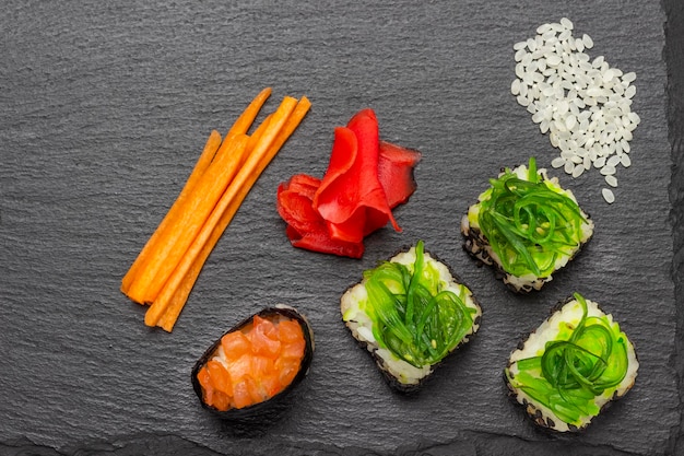 Sushi con algas verdes y salmón Arroz jengibre y zanahorias picadas sobre la mesa
