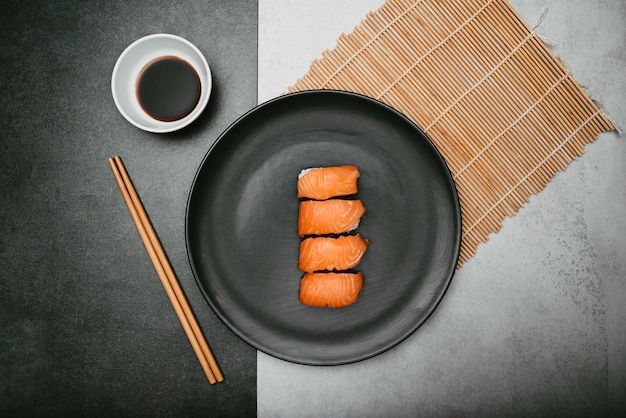 sushi de arroz nigiri de salmón japonés presentado sobre un plato negro con salsa de soja y palillos