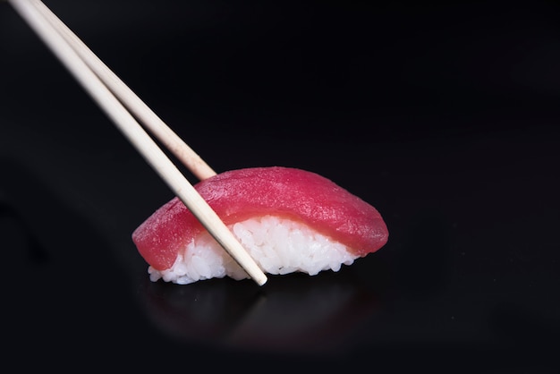 Sushi atún nigiri en palillos sobre negro