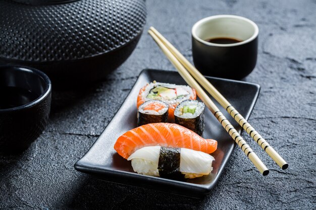 Foto sushi auf einem schwarzen teller mit stäbchen